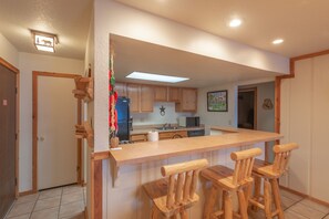 A kitchen with wooden cabinets, a central island with bar stools, a microwave, and a refrigerator. - Great location! Ski-In/Out Dog Friendly Condo w/ Fireplace & Views (Mt. Crested Butte)