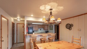 Eine Küche mit Holzausstattung, einer zentralen Kochinsel mit Barhocker, einer Kandelaberleuchte und einem Esstisch mit Stühlen.
