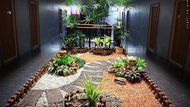A hallway with a decorative garden area featuring plants, wooden planks, and pebbles. - Merdelong Hotel (Phatthalung)