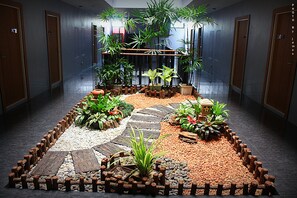 Un couloir agrémenté d’un espace jardin décoratif comprenant des plantes, des planches de bois et des galets.