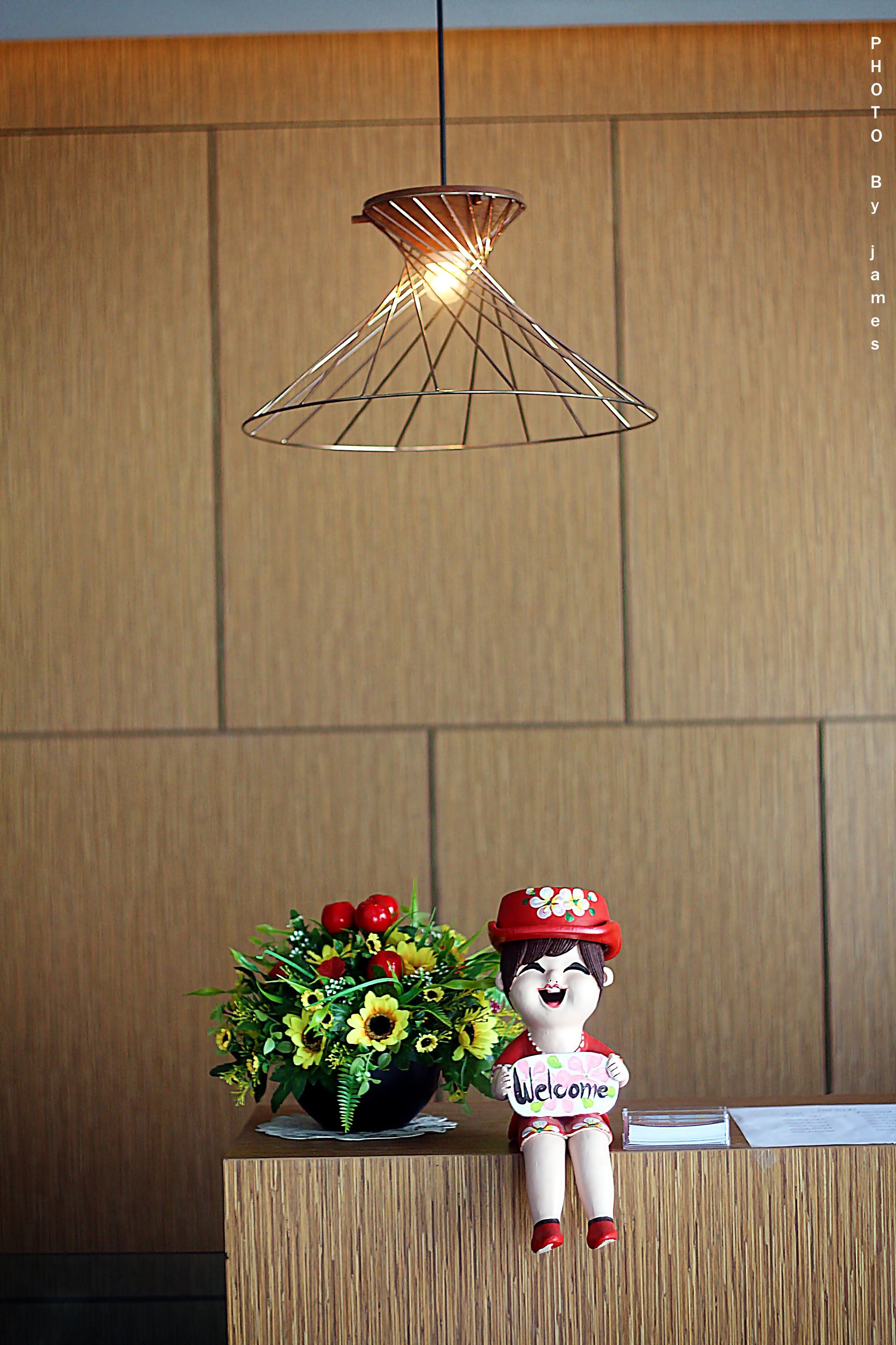 A reception desk with a decorative welcome sign, a floral arrangement, and a hanging light fixture.