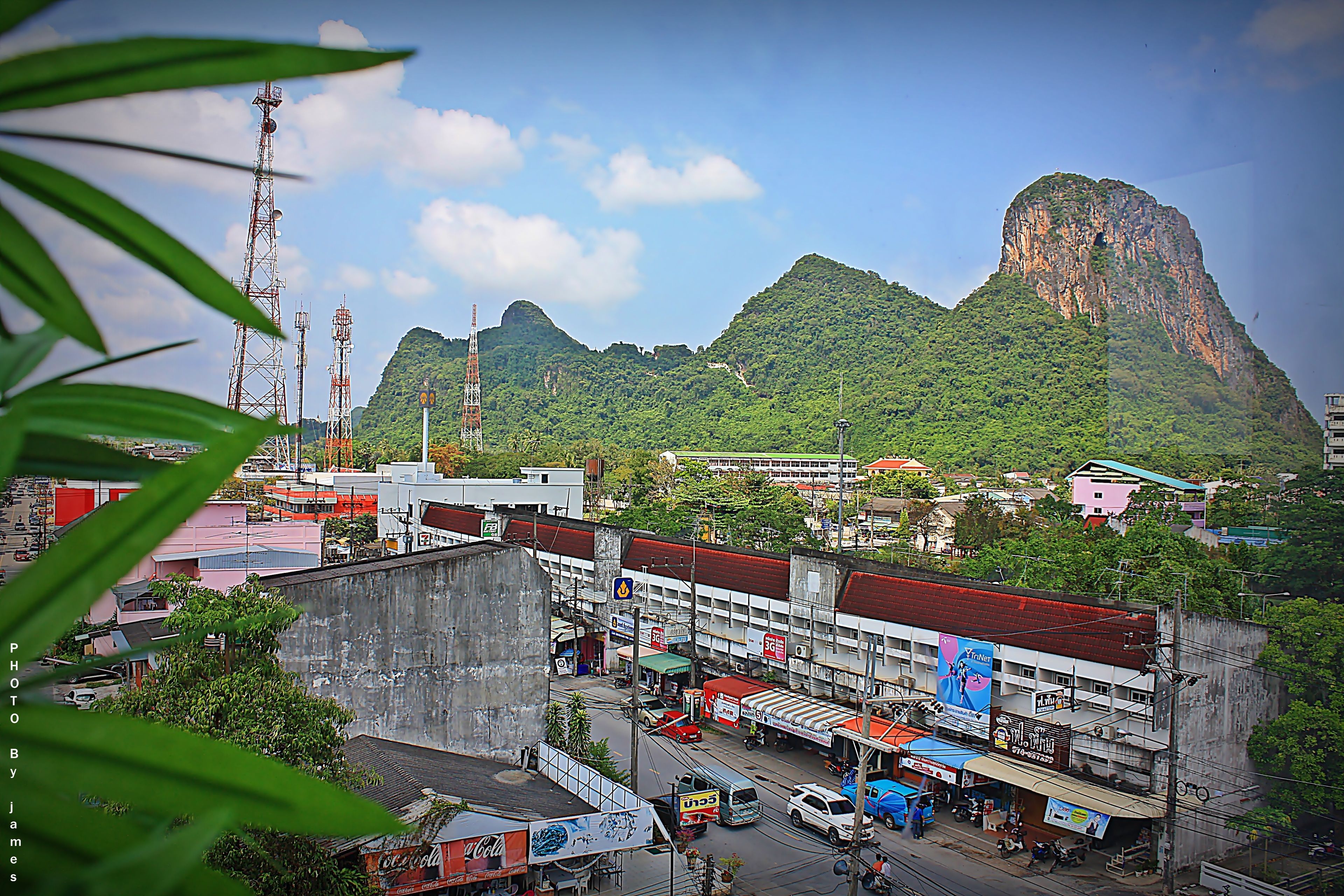 A cityscape with a prominent mountain in the background, a busy street with vehicles, and various buildings including a large commercial structure with a red roof.