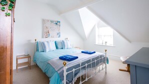 A bedroom with a sloped ceiling, a bed with blue bedding, a bedside table, and a wall-mounted artwork.