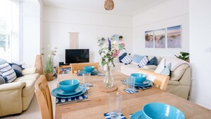 A modern living room with a wooden dining table set for four, blue bowls, and a vase with flowers.