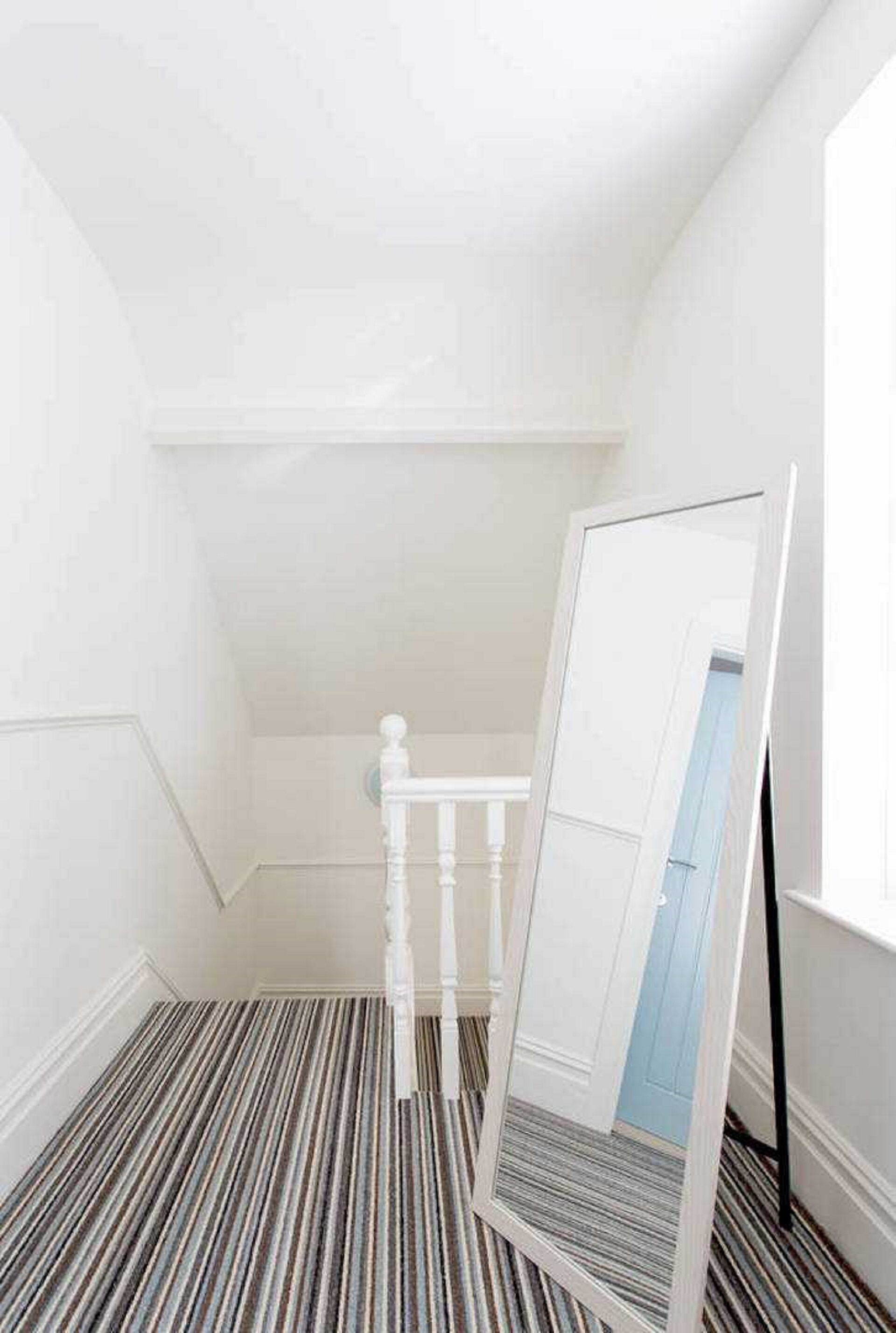 A narrow hallway with a striped carpet, a white door, and a mirror leaning against the wall.