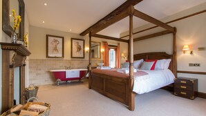 A four-poster bed with a wooden headboard, a red clawfoot bathtub, and a wooden nightstand with drawers.