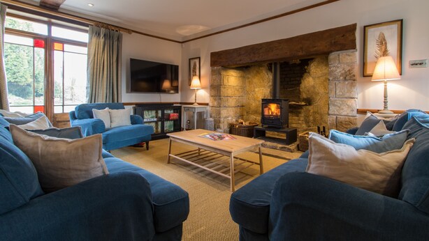A cozy living room with a stone fireplace, blue sofas, and a flat-screen TV.
