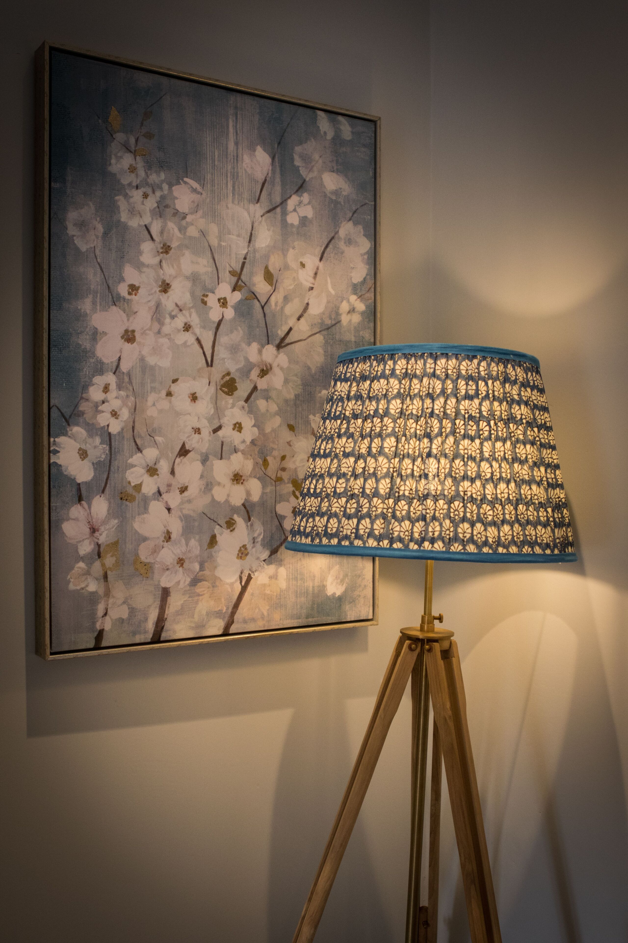 Eine Stehlampe mit einem gemusterten Lampenschirm und ein Bild von weißen Blumen an der Wand.