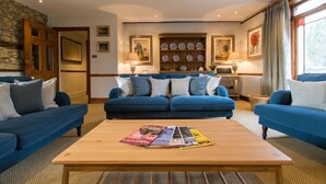 A living room with a blue sofa set, a wooden coffee table with magazines, and a stone wall.