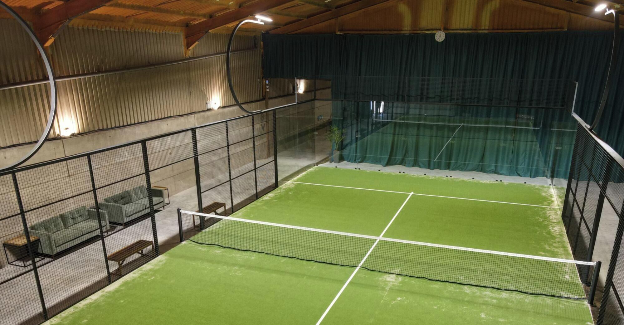 An indoor tennis court with a net, seating area, and enclosed space with a wooden ceiling.