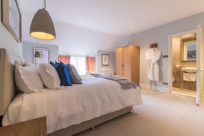 Quarto com uma cama grande, guarda-roupa de madeira, roupão pendurado na porta e um banheiro visível através de uma porta aberta.