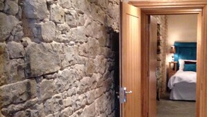 Un pasillo con pared de piedra que conduce a un dormitorio con cama y mesita de noche.