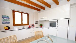 Eine moderne Küche mit weißen Schränken, einer Holzbalkendecke, einem Glastisch und einem Fenster.