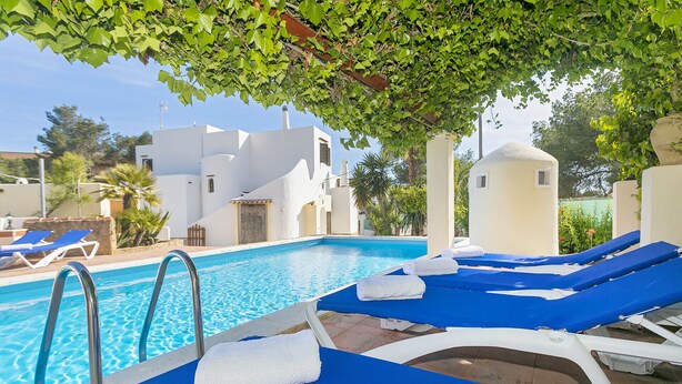 Un espace piscine avec des chaises longues bleues et des serviettes blanches, entouré de bâtiments blancs et de verdure.