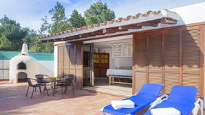 Une terrasse avec deux fauteuils de jardin bleus, une table et un petit coin cuisine extérieur.