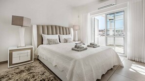 Ein modernes Schlafzimmer mit einem großen Bett, Nachttischen, einem flauschigen Teppich und Blick durch eine Glastür.