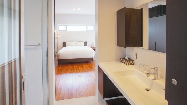 A modern hotel room with a large bed, a white vanity with a mirror, and a wooden floor. - Kariyushi Condominium Resort Onna Maeda Base (Onna)