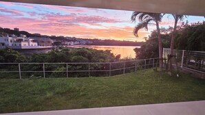 A balcony with a view of a sunset over a body of water, surrounded by greenery and a fence. - Kariyushi Condominium Resort Onna Maeda Base (Onna)