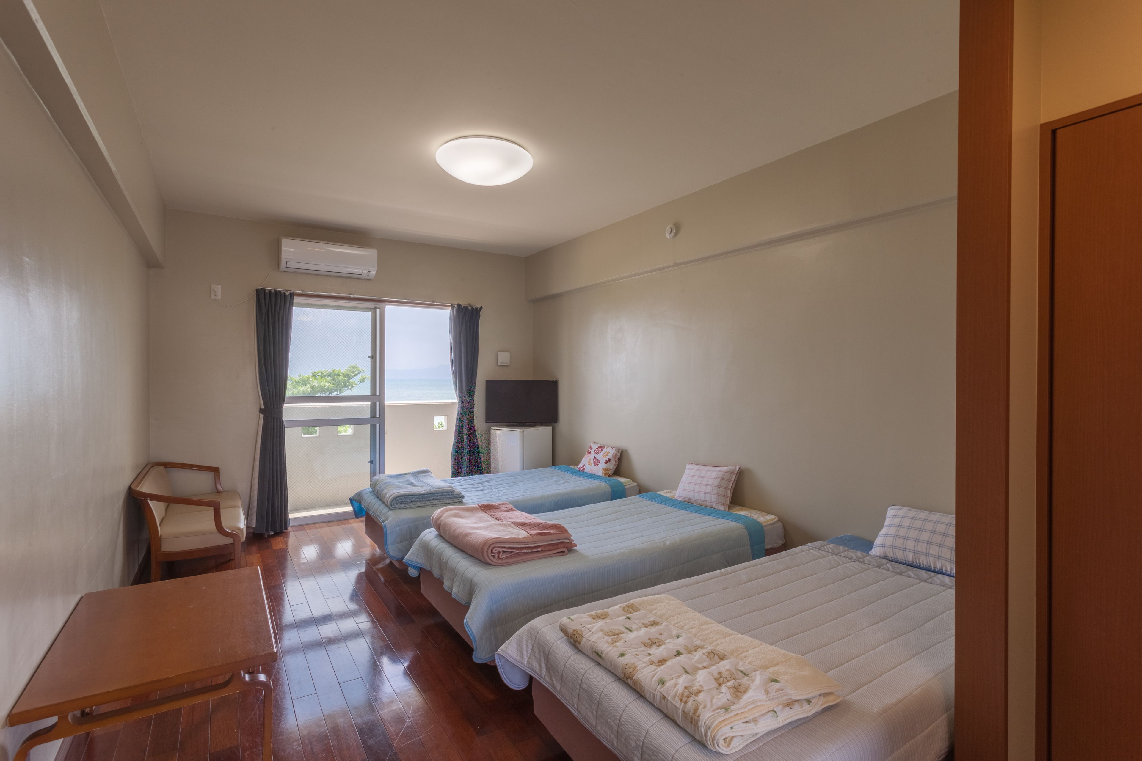 Ein Hotelzimmer mit zwei Betten, einem Holztisch, einem Fernseher und einem Balkon mit Blick.