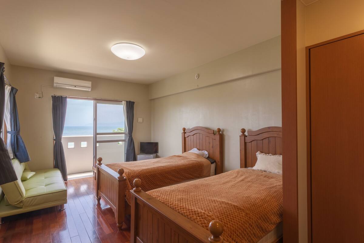 Quarto de hotel com duas camas de madeira, um sofá e uma varanda com cortinas.