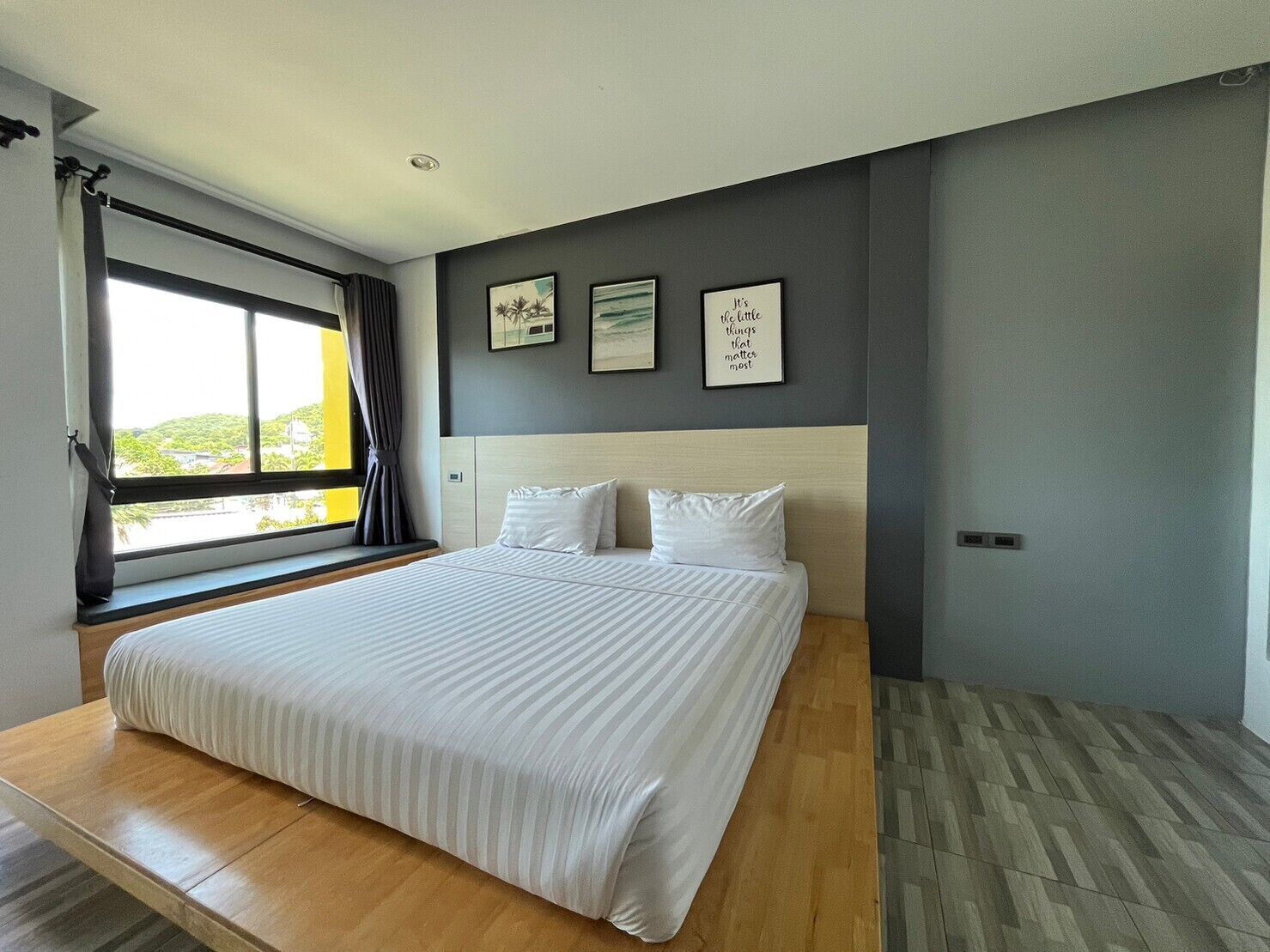 A modern bedroom with a large bed, a view through a sliding door, and three framed pictures on the wall.
