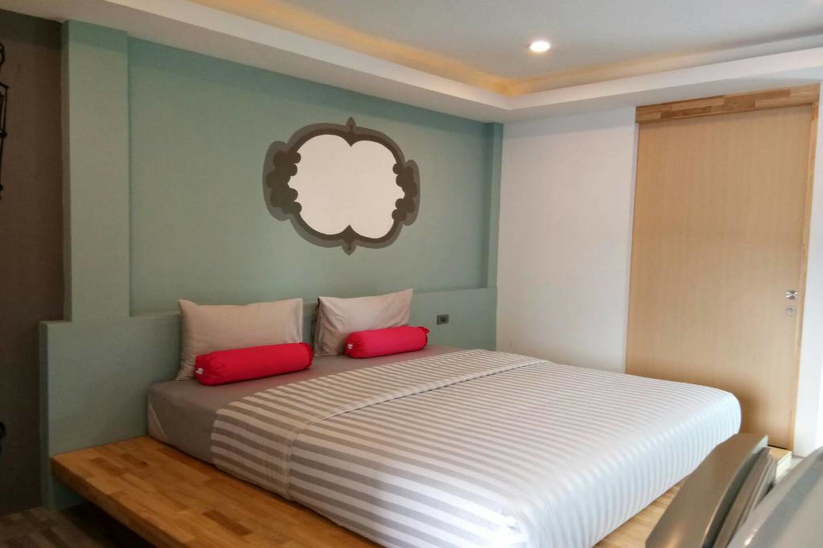 A bedroom with a bed, two pillows, a bedside table, and a wall-mounted mirror.