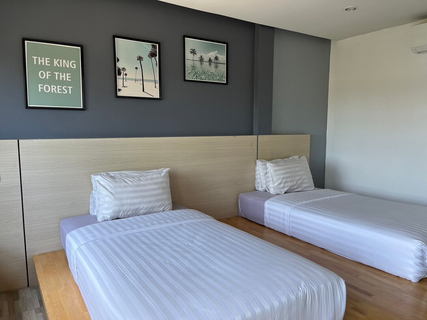 A hotel room with two single beds, a grey headboard, and three framed pictures on the wall.