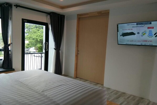 Habitación de hotel con cama, puerta y televisor empotrado mostrando un menú tailandés.