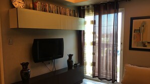 Ein Wohnzimmer mit Flachbildfernseher, einer Bücherwand voller Bücher, einer Vase und einem fenster mit Vorhängen.