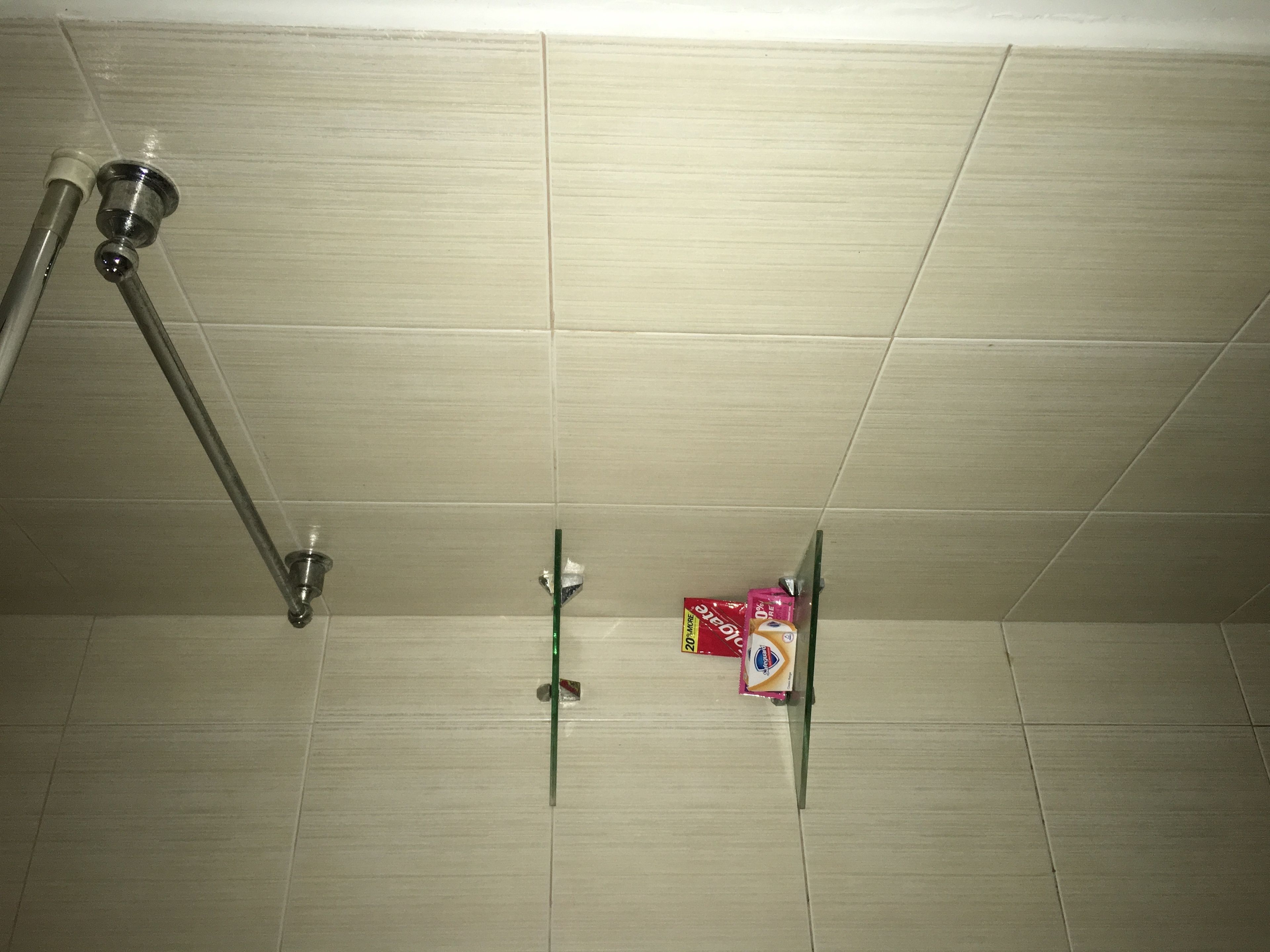 Une salle de bain avec des carreaux blancs, une pomme de douche et un distributeur de savon fixé au mur.