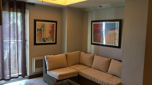 Ein Wohnzimmer mit einem beigefarbenen Ecksofa, einem Glastisch, Deckenventilator und zwei gerahmten abstrakten Bildern.