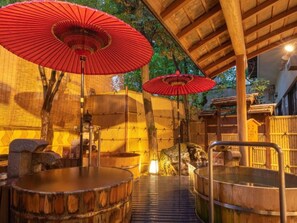 A traditional Japanese onsen with wooden benches and red umbrellas, surrounded by bamboo walls and wooden structures. - Ryokufukaku (Toyooka)