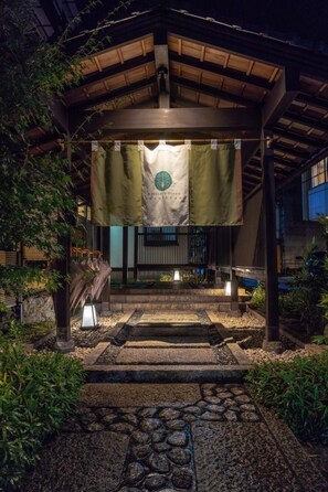 A traditional Japanese-style entrance with a wooden structure, a stone pathway, and a hanging banner with a logo. - Ryokufukaku (Toyooka)