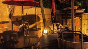 Un onsen japonais traditionnel, avec des bains en bois et un parasol rouge.
