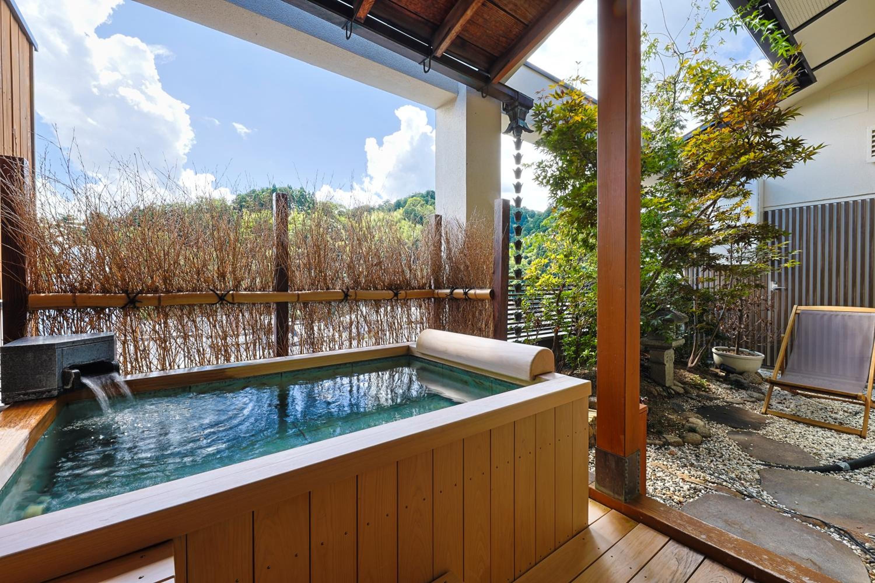 A wooden hot tub with a view of a bamboo fence and trees.