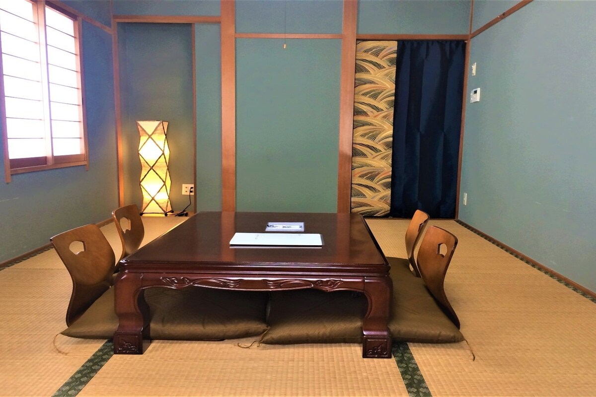 A conference room with a wooden table, cushioned chairs, a decorative lamp, and patterned curtains.