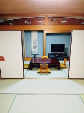 A traditional Japanese room with tatami flooring, a low table, cushions, and a television. - Hotel Yamacho (Ako)