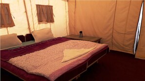 A single bed with a patterned blanket, a bedside table with a bottle, and a window with curtains. - TIH The Norling Camp - Pangong (Leh)