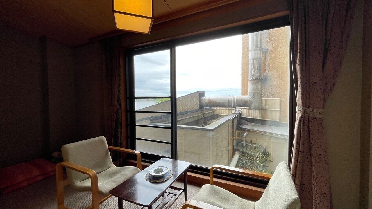 Una habitación con un ventanal grande, dos sillas, una mesita y vistas a un edificio.