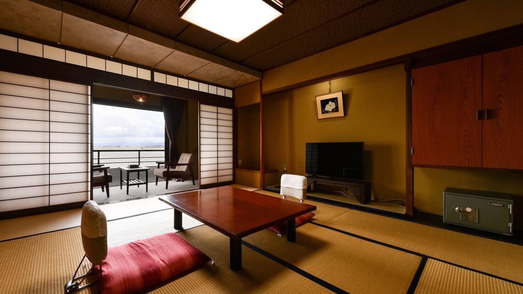 A traditional Japanese room with tatami flooring, a low table, a sofa, a TV, and a view of the sea.