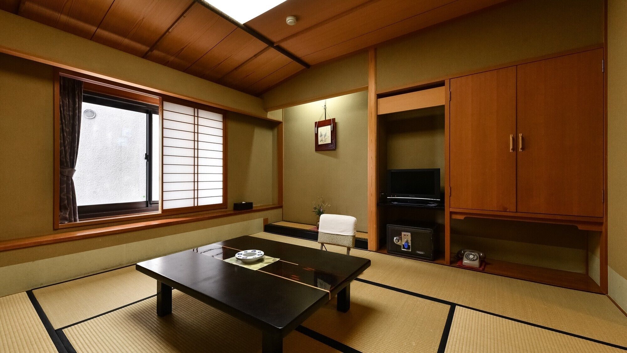 A traditional Japanese room with tatami flooring, a low table, a TV, and wooden cabinets.