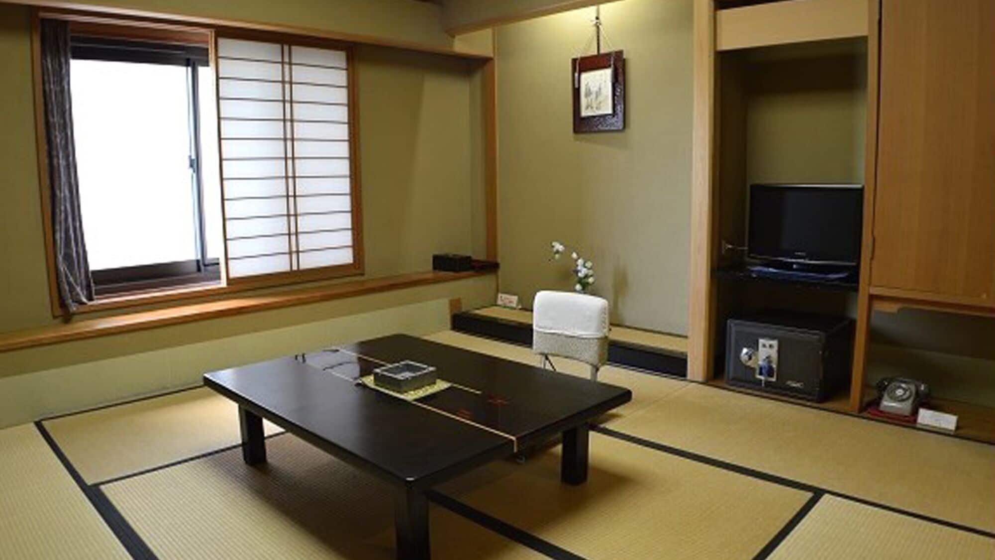 Una habitación con tatami, una mesa baja, una silla, un televisor y una estantería con objetos.