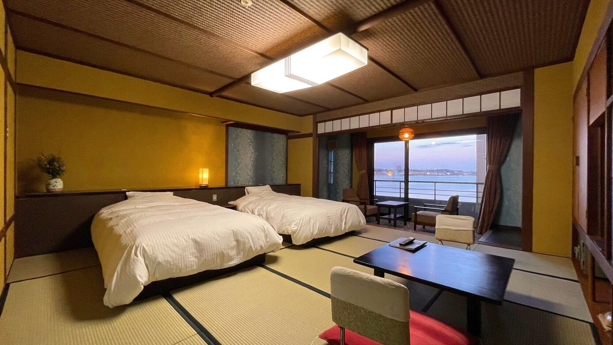 Habitación de hotel con dos camas, una mesita, una silla, vista al mar y un diseño de techo tradicional.