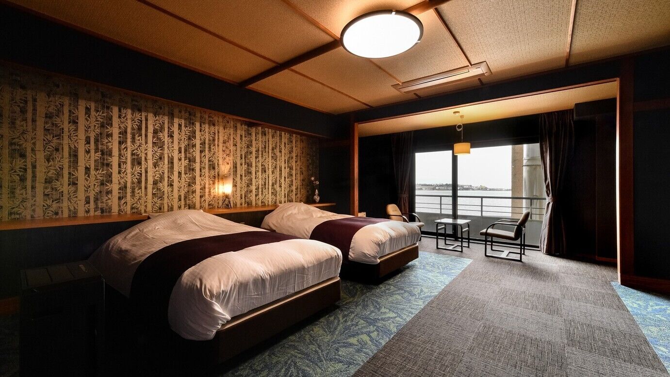 A hotel room with two beds, a small table, a chair, and a view of the water.