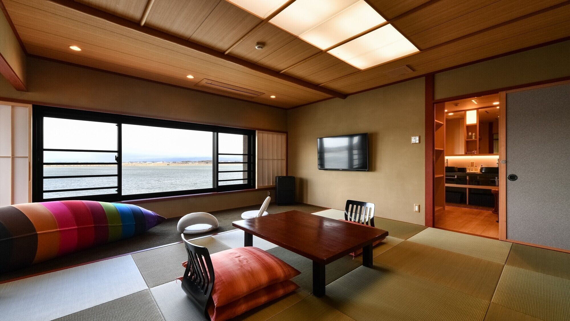 A room with tatami flooring, a television, a dining table, and a view of the sea.