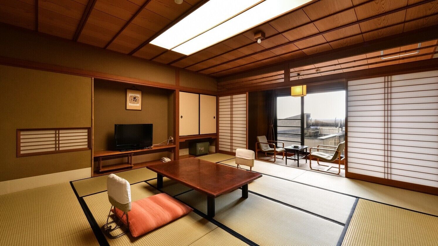 A traditional Japanese room with tatami flooring, a low table, a television, sliding doors, and a view of the city.