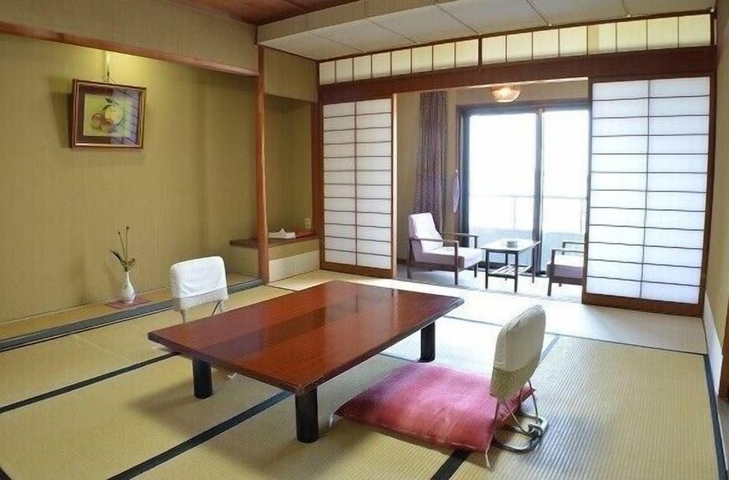 Una habitación tradicional japonesa con suelo de tatami, una mesa de madera baja, una silla blanca y un shoji corredizo.