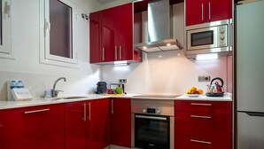 Une cuisine moderne avec des meubles de couleur rouge, des appareils en acier inoxydable et un plan de travail blanc.