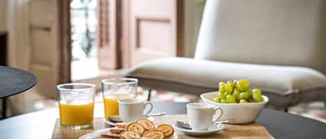 A breakfast setting with a plate of pastries, glasses of orange juice, a bowl of grapes, and a white cup on a table.