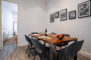 A dining area with a wooden table set for four, grey chairs, and a bowl of fruit.